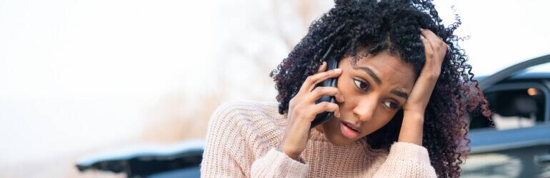 stressed woman with head in hand making a phone call in front of her car