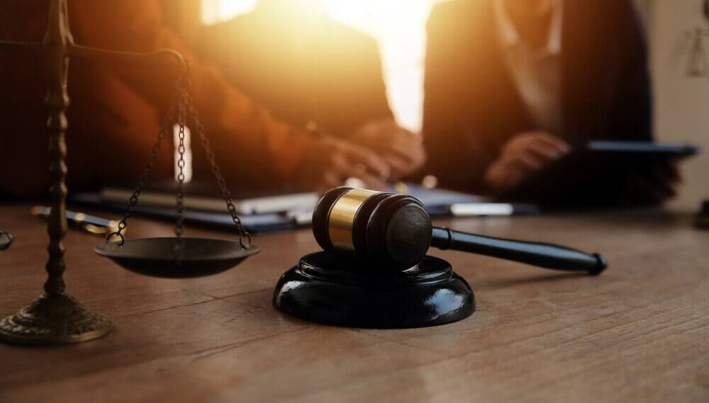 Gavel and scales of justice on desk with Greensboro personal injury attorneys discussing a case in the background.